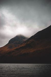 Scenic view of sea by mountain against sky