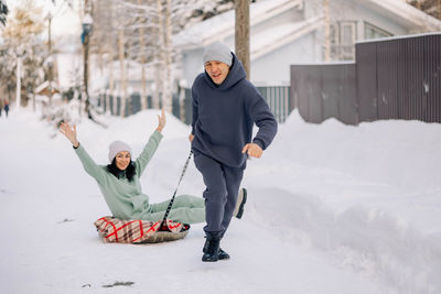 Smiling man giving sledding ride to woman. love and leisure concept.