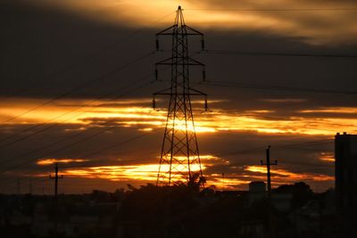 Low angle view of silhouette electricity pylon against dramatic sky during sunset