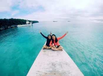 Portrait of happy friends sitting on boat in sea against sky