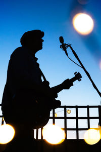 Silhouette people playing guitar against blue sky