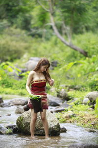 Full length of woman standing on rock in forest