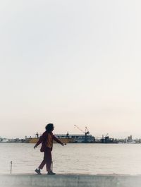 Rear view of woman standing on shore against clear sky