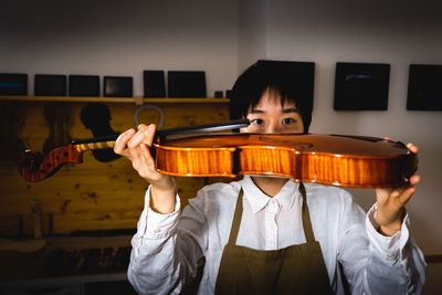 Young chinese woman violin maker checking the quality of her violin in the workshop