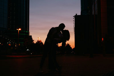 Silhouette couple kissing while standing in city during sunset