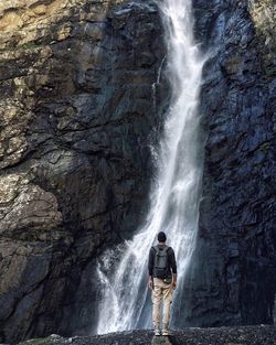 Rear view of man standing in front of waterfall