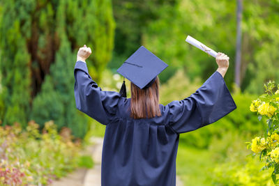 Rear view of woman in graduation gown walking on footpath at park