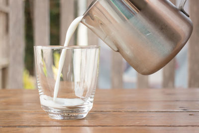 Close-up of jug pouring milk in glass on wooden table