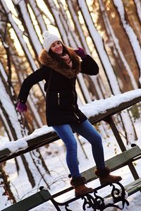 Portrait of young woman standing on bench during winter