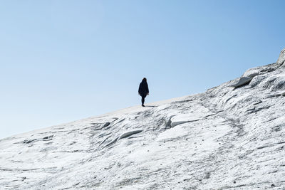 Low angle view of man standing on mountain against clear sky