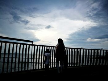 Rear view of woman standing on railing against sky