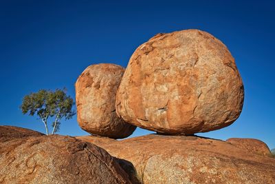 Low angle view of devils marbles formation against clear blue sky