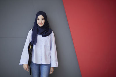 Portrait of young woman standing against wall