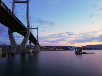 View of suspension bridge over river against cloudy sky