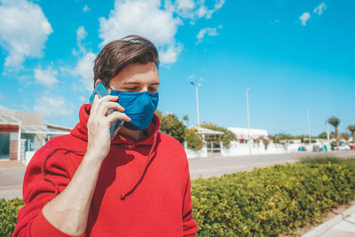 Portrait of young man holding camera against sky