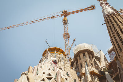 Low angle view of crane by building against sky