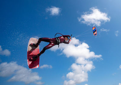 Low angle view of person kiteboarding against blue sky