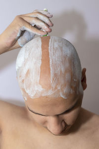 Close-up of man shaving head against white background