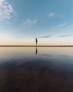 Woman standing on beach against sky during sunset