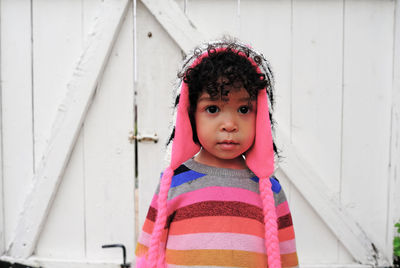 Portrait of cute girl wearing warm clothing standing against white wooden wall