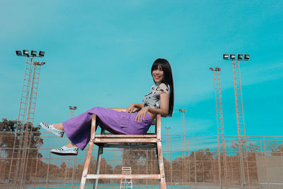 Low angle portrait of woman sitting on chair against clear blue sky