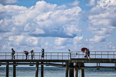 People on footbridge over river against sky