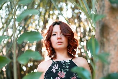 Portrait of beautiful young woman standing against plants