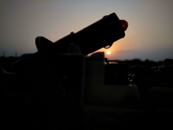 Close-up of silhouette holding camera against sky during sunset