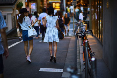 Rear view of people walking on street by bicycles in city