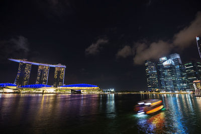 Illuminated buildings by river against sky at night