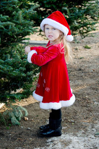 Child dressed in red santa outfit looks a little disgruntled as she picks out a christmas tree