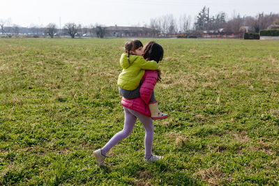 Small child riding piggyback on elder sister outdoors in the field