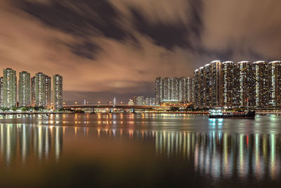 Illuminated buildings by sea against sky at night