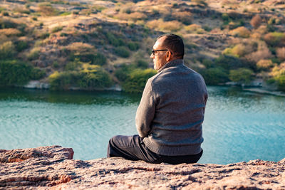 Isolated man sitting at mountain top with lake view from flat angle