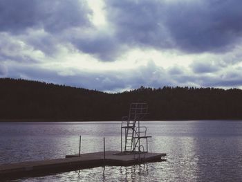 Boats in calm lake against cloudy sky