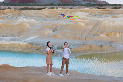 A boy and girl launch a bright kite into the sky in the mountains near the river.