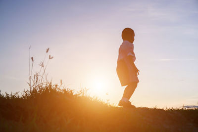 Woman standing on field against sky during sunset