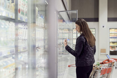 Rear view of woman looking at packet by display cabinet in supermarket