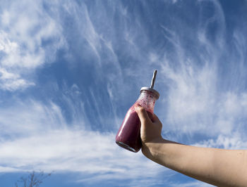 Low angle view of person holding smother against sky