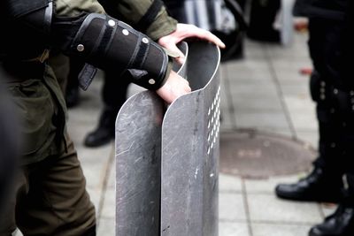 Midsection of police officer holding shield on footpath during protest