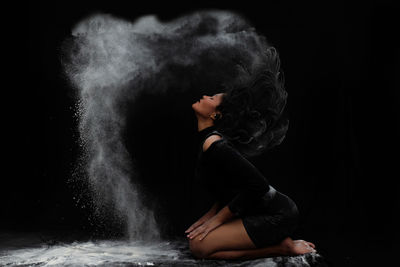 Side view of woman dancing against black background