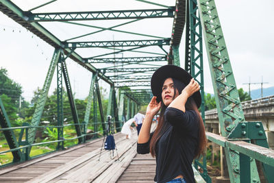 Side view of woman wearing hat standing on footbridge