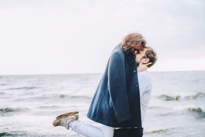 Mid adult man holding sunglasses while standing on beach