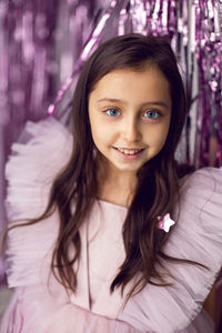 Beautiful girl with big eyes in a pink dress stands against the background of new year's tinsel