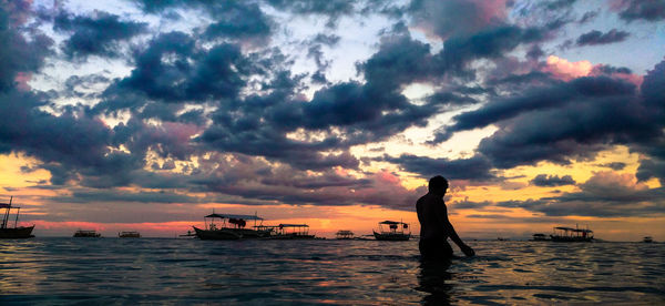 Silhouette people on sea against sky during sunset
