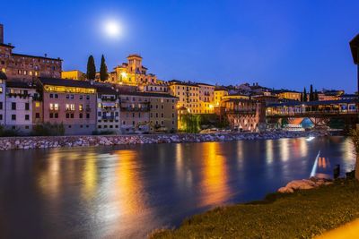 Illuminated buildings by river against sky at night