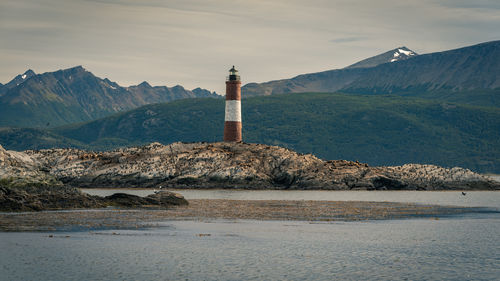 Lighthouse by sea and mountain against sky