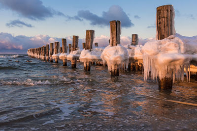 Frozen wooden posts in sea against sky