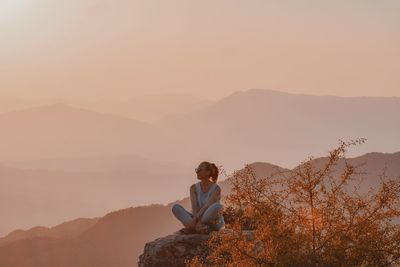 Man sitting on rock against mountain range