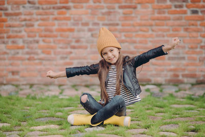 Full length of girl wearing hat sitting against wall